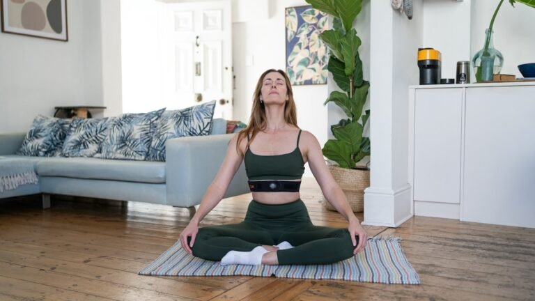 Woman sitting cross-legged on a mat at home, breathing with her eyes closed
